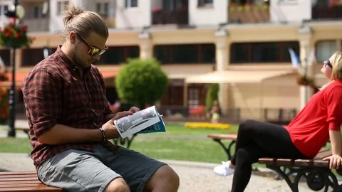 Young man sitting on the bench and reading absorbing book Video stock 77474181