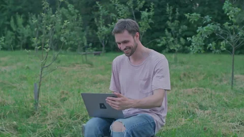 A young man is sitting on a bench and working on a laptop.Red Helium 8K Stock Footage 156204721