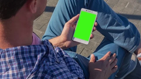 Young Man sitting on the bench in city park holds SmartPhone Stock Footage 81204643