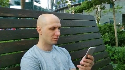 Young man sitting on bench in city park and using mobile phone Stock Footage 201891864