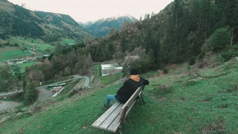 Young man sitting on a bench with a view in a snowy mountain valley, Alps Stock Footage 272262865