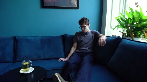 Young Man sitting on a big Sofa grabbing Tea Stock Footage 274188274