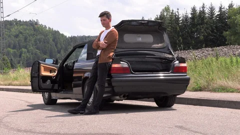 A young man is sitting by a broken car on the road 動画素材 113388789