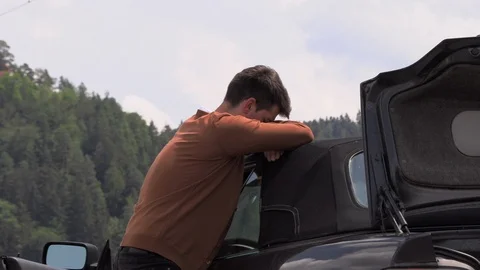 A young man is sitting by a broken car on the road 库存影片 113389039