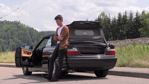 A young man is sitting by a broken car on the road Видео 113567715