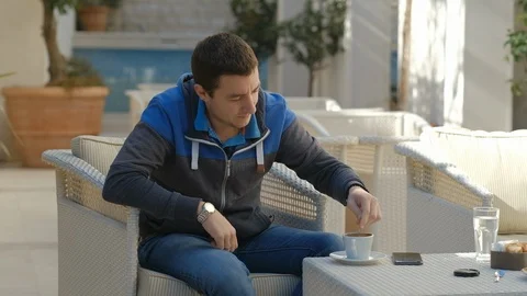 Young man sitting in a cafe alone outdoors and drinking coffee in the morning Stock Footage 126053532