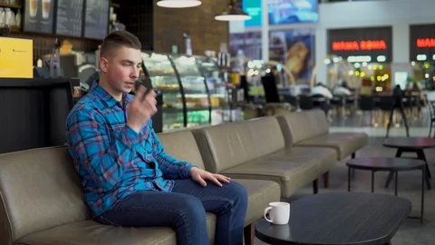 A young man is sitting in a cafe and talking on the phone. A man is talking on Stock Footage 125636125