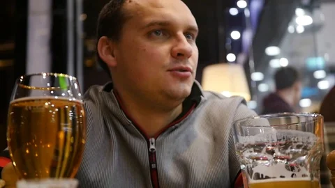 A young man is sitting in a cafe, drinking beer talking to friends, telling Stock Footage 85795276