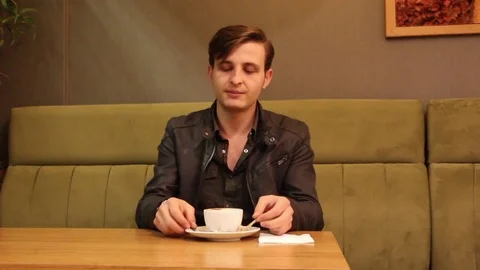 Young man sitting at cafe enjoying music while drinking coffee Stock Footage