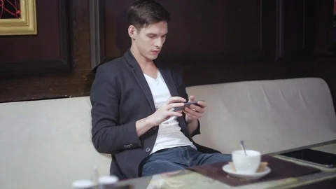 Young man sitting in a cafe playing a game on your smartphone Stock Footage 75695462