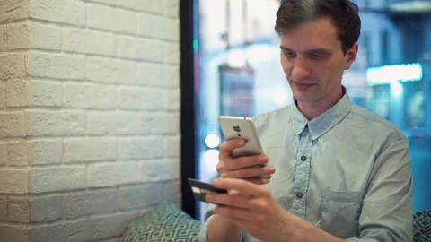 Young man sitting in cafe, using smartphone and credit card for shopping on net Stock Footage 77168810