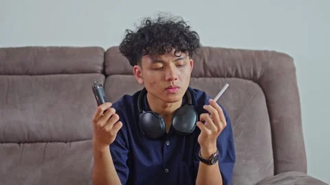 Young man sitting choosing vape device comparing electronic vape and cigarette Stock Footage 332389008