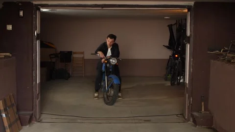 Young man sitting on a classic blue motorcycle, looking at the camera, parked Stock Footage 342772588