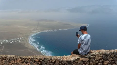 Young man sitting on a cliff wall in Lanzarote Stock Footage 136824901