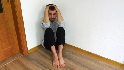 A young man is sitting in the corner of the room on the floor. Out of sorts Stock Footage 134643740