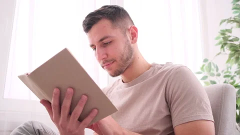 Young man sitting on couch and reading book Stock Footage 171545250