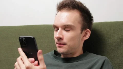 Young man sitting on a couch engaged in conversation on a smartphone Stock Footage 301521083