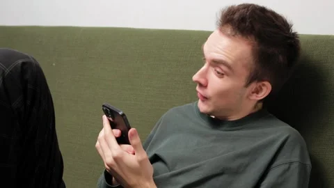 Young man sitting on a couch engaged in conversation on a smartphone Stock Footage 301521148