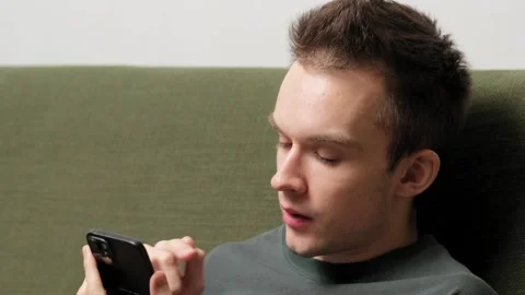 Young man sitting on a couch engaged in conversation on a smartphone Stock Footage 301521505