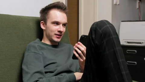 Young man sitting on a couch engaged in conversation on a smartphone Stock Footage 301521993
