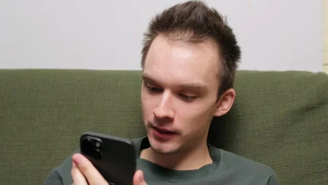 Young man sitting on a couch engaged in conversation on a smartphone Stock Footage 301522065