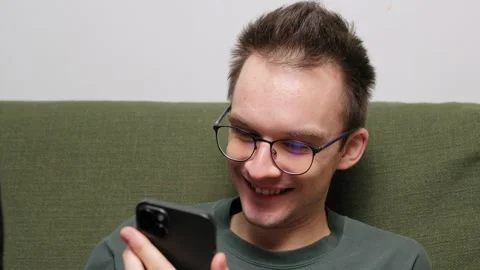 Young man sitting on a couch engaged in conversation on a smartphone Stock Footage 301522202
