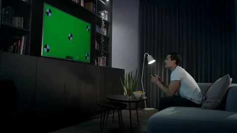 A young man sitting on a couch at home playing a video game. Track left to right Stock Footage 100194967
