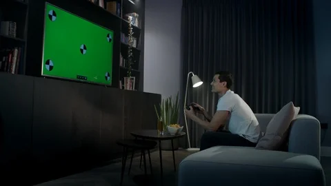 A young man sitting on a couch at home playing a video game. Camera track right  Stock Footage 100195904