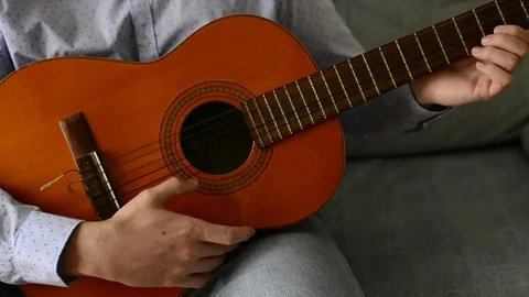 Young man sitting on the couch at home and playing the guitar. Spanish guitar Stock Footage 129267826