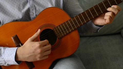 Young man sitting on the couch at home and playing the guitar. Spanish guitar Stock Footage 129267847