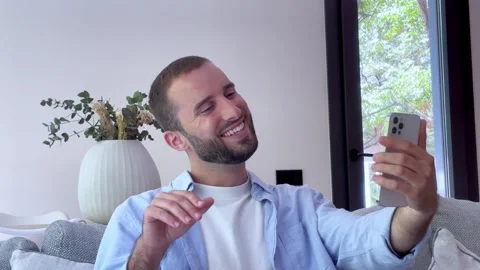 Young man sitting on a couch at home, smiling and gesturing while talking Stock Footage 345113535