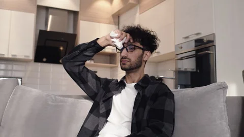 Young man sitting on a couch in a kitchen, looking at the thermometer and Stock Footage 273229679
