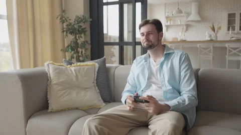 Young Man Sitting on Couch Playing Video Games at Home in Apartment Stock Footage 303086396