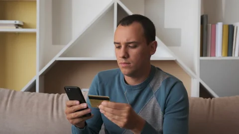 Young man sitting on the couch, using smart phone for online shopping Stock Footage 134872809
