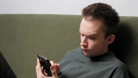 Young man sitting on a couch using smartphone Stock Footage 301521133