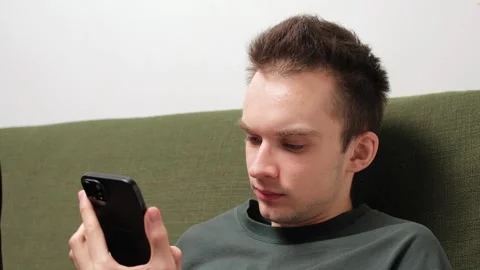 Young man sitting on a couch using smartphone Stock Footage 301521318