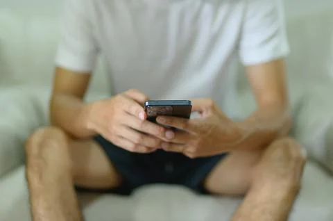 Young Man Sitting on Couch Using Smartphone with Focus on Hands and Device 스톡 사진