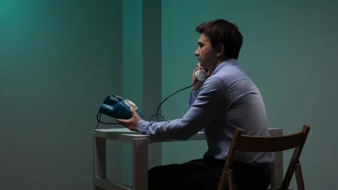 Young man sitting at a desk and dialing a number on a blue retro push button Stock Footage 345532199