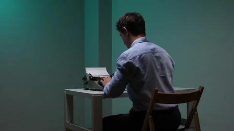 Young man sitting at a desk, focused on typing a manuscript on an old fashioned Stock Footage 345529877
