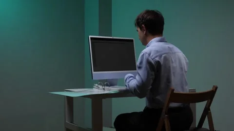 Young man sitting at a desk, typing on a computer keyboard in a dimly lit Stock Footage 344605277