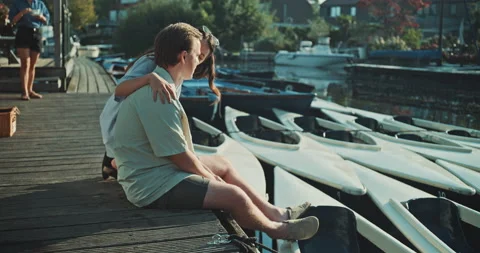 Young man sitting on the dock then girl approaching him Stock Footage 221317841
