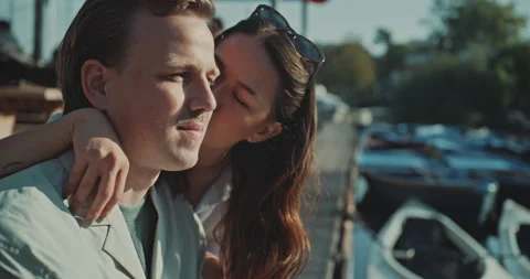Young man sitting on the dock when girl kissing him on the cheek Stock Footage 221317752