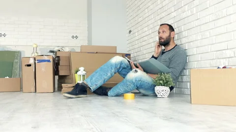 Young man sitting with documents on floor at his new home, 4K Vídeo Stock 65384465