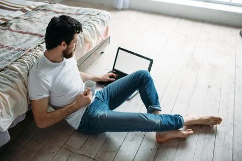 Young man sitting down on the floor near the bed Stock Photos