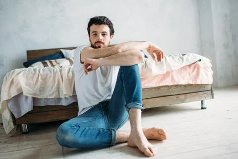 Young man sitting down on the floor near the bed Stock Photos