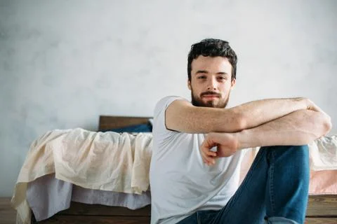 Young man sitting down on the floor near the bed Foto stock
