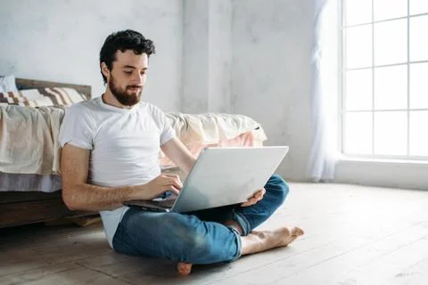 Young man sitting down on the floor near the bed Stock Photos