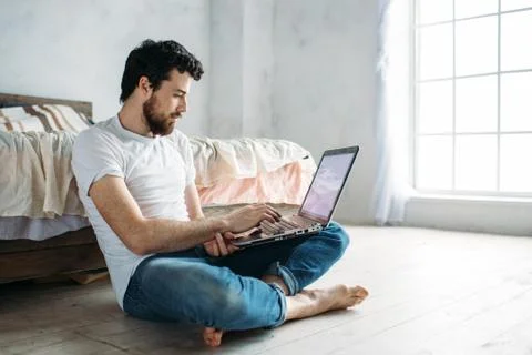 Young man sitting down on the floor near the bed Stock Photos