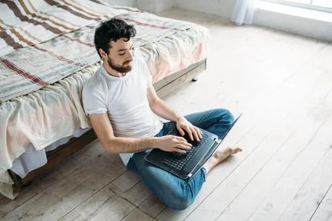 Young man sitting down on the floor near the bed Stock Photos
