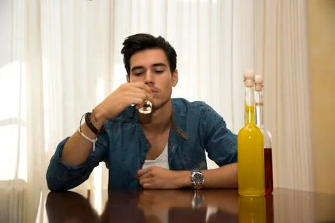 Young man sitting drinking alone at a table with two bottles of liquor Stock Photos